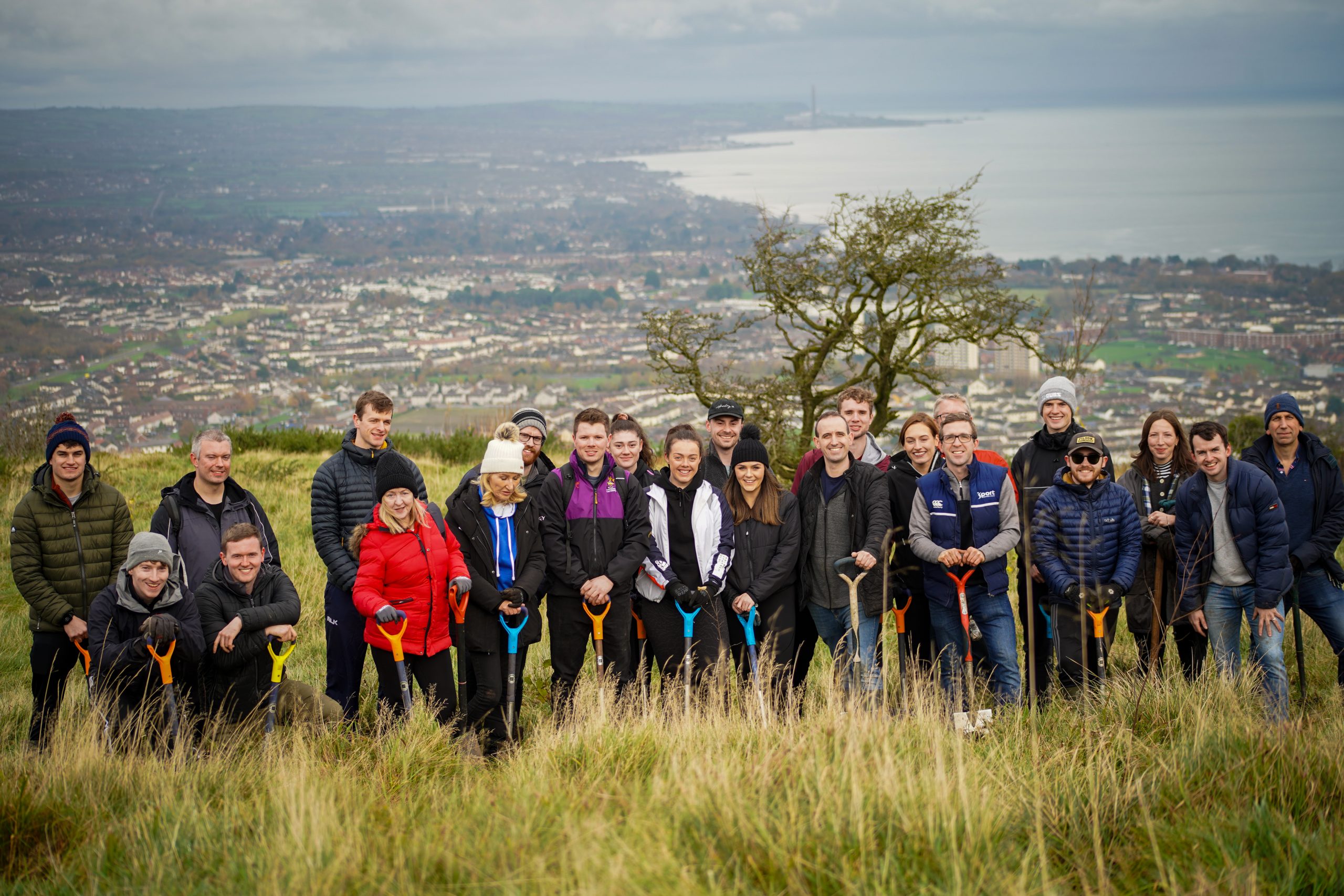 Group of employer supported volunteers holding spades, standing on top of a hill